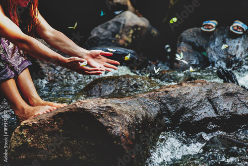 Obraz na plátne Softly flowing water frames the tranquil moment where gentle hands reach out, inviting colorful butterflies while the sunlight dances upon the surface
