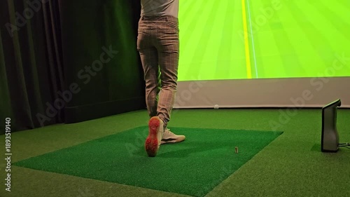 Golf practice session indoors on a simulator with a player preparing to swing