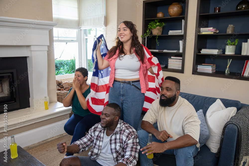 Naklejka premium Diverse friends cheering and draping american flag, holding glass bottles in cozy living room