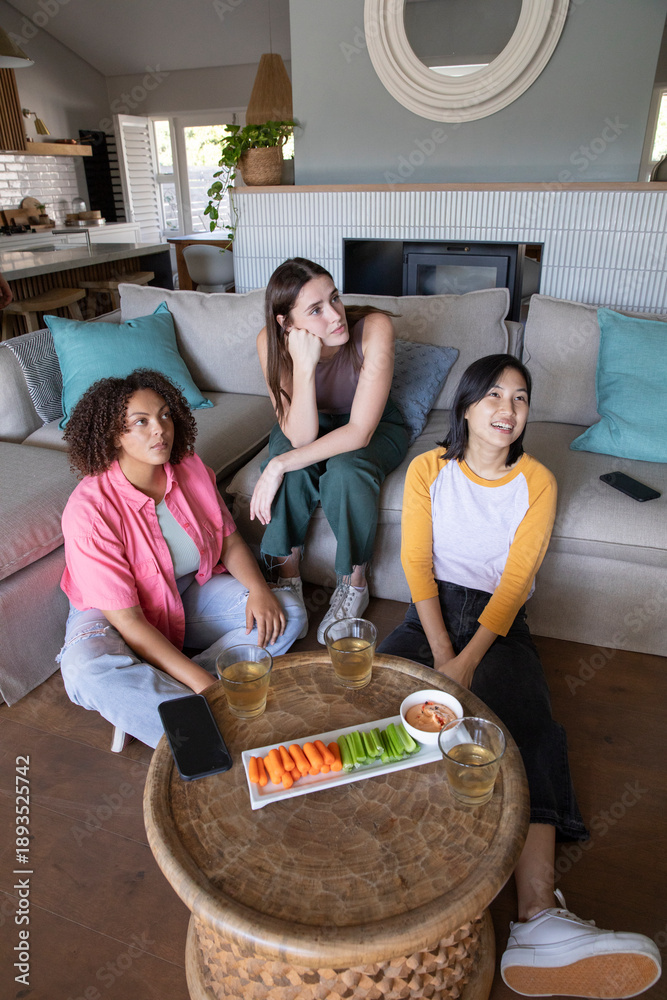 Obraz premium Diverse female friends chatting around coffee table in living room with veggie platter, smartphones