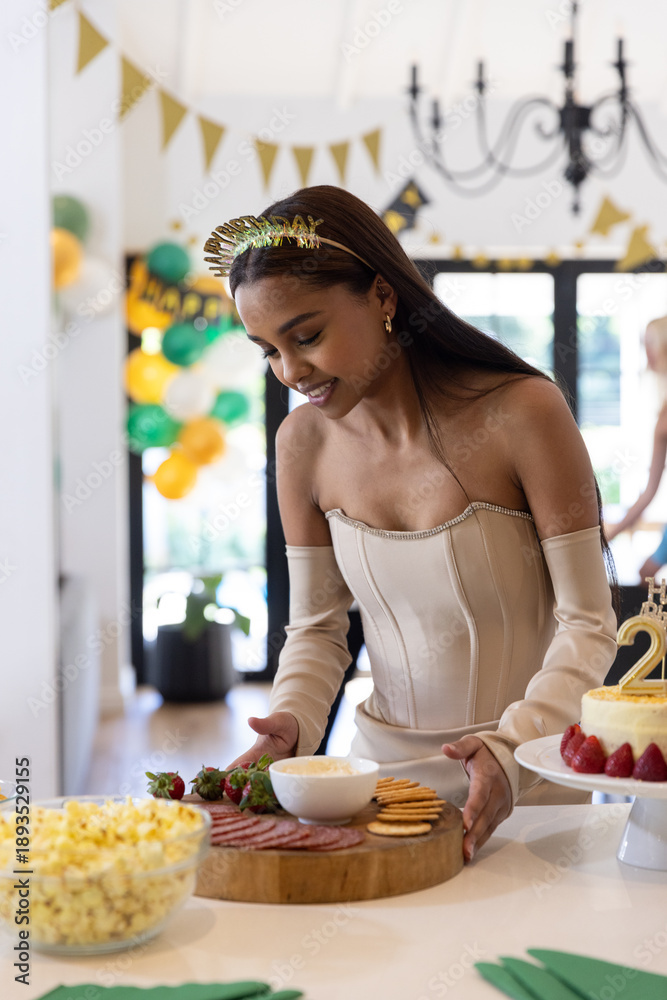 Naklejka premium African american woman wearing strapless dress arranging buffet at home with charcuterie, cake