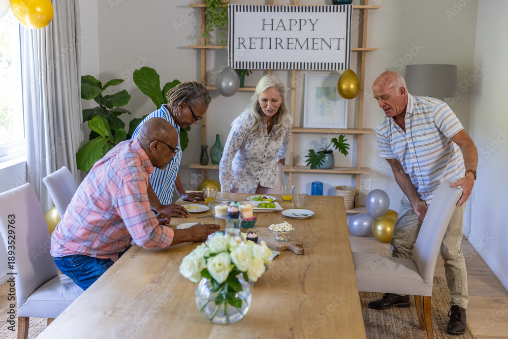 Fototapeta premium Diverse senior coworkers preparing retirement party table in dining room with cupcakes, balloons