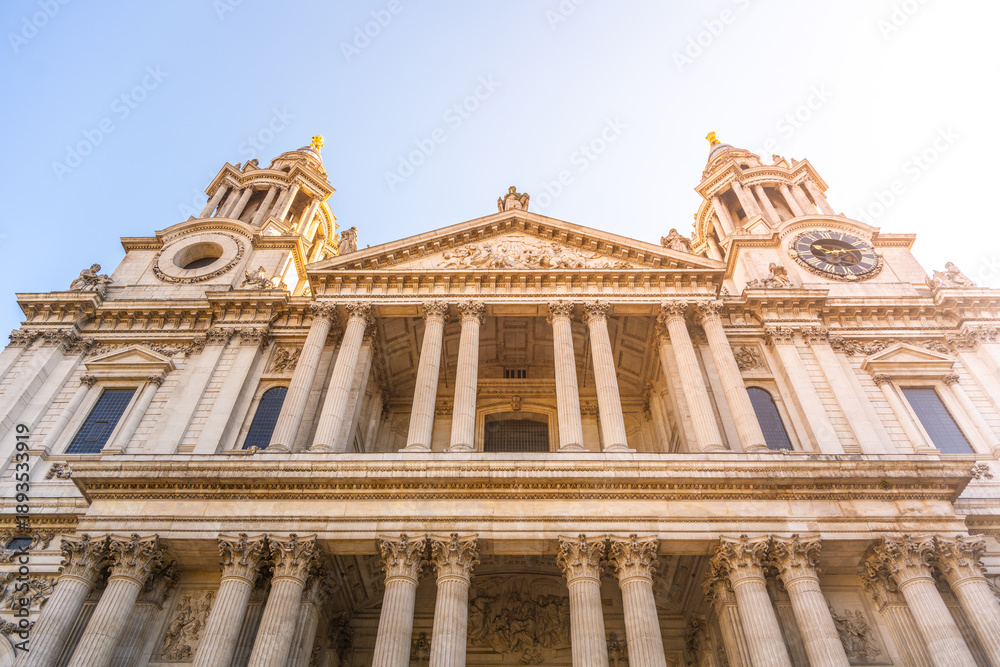 Fototapeta premium St. Pauls Cathedral stands tall in London. Visitors gather around the front portal. The sun shines on the historic building, highlighting its impressive architecture.