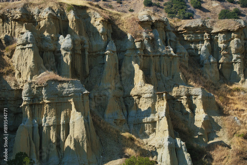 Fairy chimneys at Kula, Turkey. Impressive rock formations on a hillside, surrounded by lush greenery, highlighting the natural beauty and rugged terrain of the landscape.