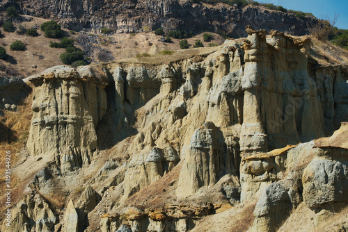 Fairy chimneys at Kula, Turkey. Impressive rock formations on a hillside, surrounded by lush greenery, highlighting the natural beauty and rugged terrain of the landscape.