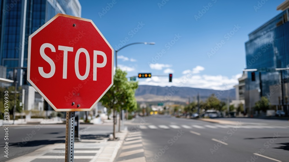 Fototapeta premium Red stop road sign at urban street intersection with modern buildings and clear blue sky. image represents traffic safety, regulation, control and urban infrastructure