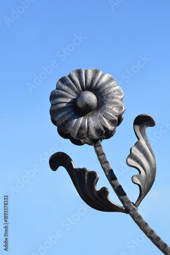 Canvastavla A decorative black wrought iron flower with leaves sits against a clear blue sky