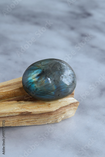 Polished labradorite stone with iridescent blue and green reflections, placed on a natural wooden base with a neutral background.