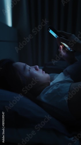 Asian woman lying in bed scrolling on her smartphone before bedtime, enjoying short-form video content on a digital platform