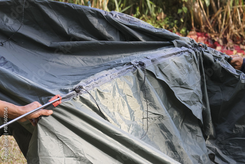 Close up outdoor shot showing hand holding pole to set up black waterproof camping tent flysheet in nature with focused preparation for overnight shelter adventure