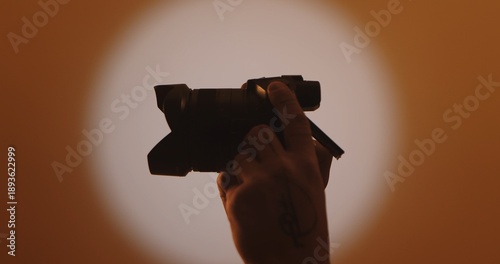 Obraz na plátne A silhouette of a hand holding a camera against a warm, softly lit backdrop, capturing the essence of photography