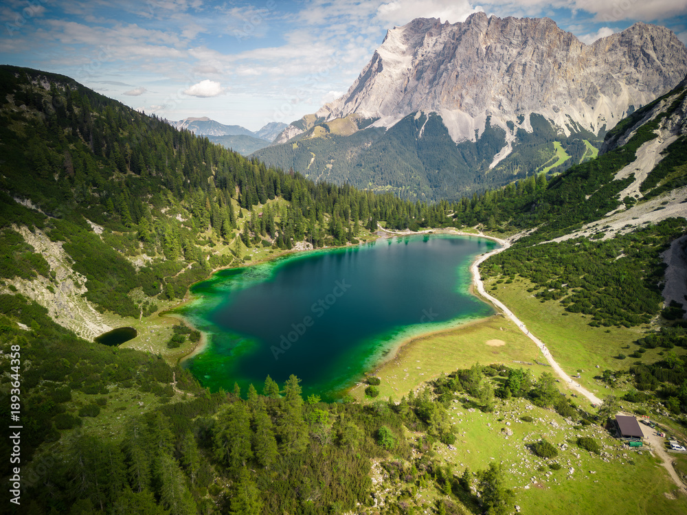 Obraz premium Stunning aerial view of turquoise alpine lake surrounded by lush green forest and dramatic mountain peak in Austrian Tyrolean Alps perfect for travel adventure and nature wall art photography themes