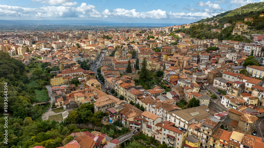 Fototapeta premium Aerial view of the town of Lamezia Terme, in the province of Catanzaro, Calabria, Italy. In the foreground, the houses of the historic center. In background, the Calabrian coast of the Tyrrhenian sea.