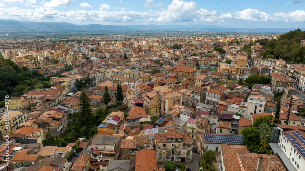 Fototapeta premium Aerial view of the town of Lamezia Terme, in the province of Catanzaro, Calabria, Italy. In the foreground, the houses of the historic center. In background, the Calabrian coast of the Tyrrhenian sea.