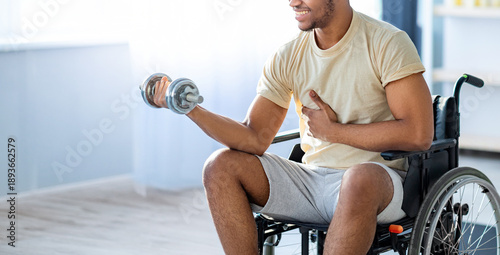 Canvas Print A young Black man using a wheelchair exercises by lifting a dumbbell in a well-lit indoor space