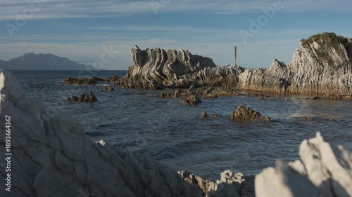 A unique rock formations, emerging from the ocean on a sunny afternoon, while low waves are kissing the rocks, and high mountains are at the distance. a 4K video clip, Kaikoura, New Zealand.