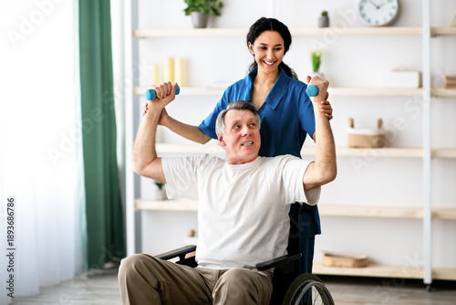 Fotografie A man using a wheelchair lifts weights with guidance from a healthcare worker in a well-lit therapy space