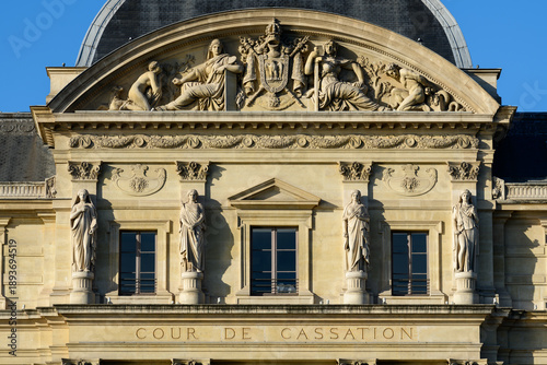 Obraz na plátně Detailed view of classical stone statues and ornate reliefs adorning the pediment and facade of the Cour de Cassation in Paris, illuminated by crisp sunlight against a vivid blue sky