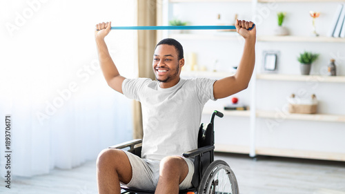 Tableau sur toile A man with dark skin is smiling while exercising in a wheelchair using a resistance band in a bright room