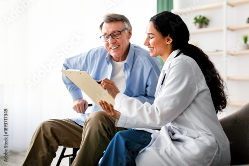 Photography A woman in a white coat shares information on a clipboard with an older man in glasses