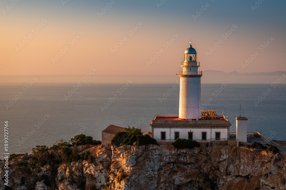 Fototapeta premium Mallorca, Spain - Aerial view of the Lighthouse at Cap de Formentor at sunrise with warm sunlight and golden and blue sky