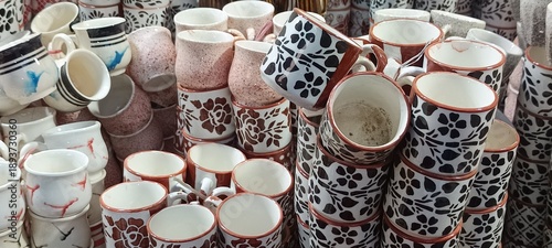 These are stacks of ceramic tea cups and mugs. 
They feature various designs, including solid colors and distinct black and brown floral patterns. 
