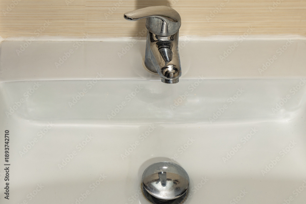 Fototapeta premium Water leaking from the tap into the sink, dripping clean water, data leak, bathroom faucet