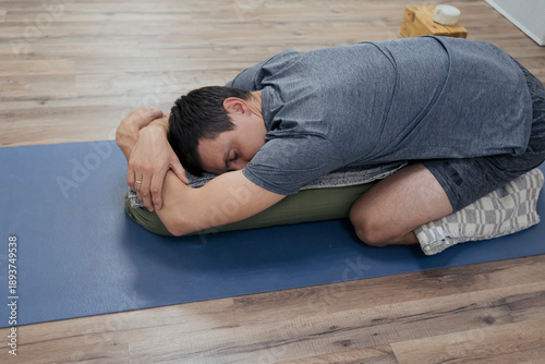 Billede på lærred man doing variation of child pose using bolster and other props relaxing at yoga