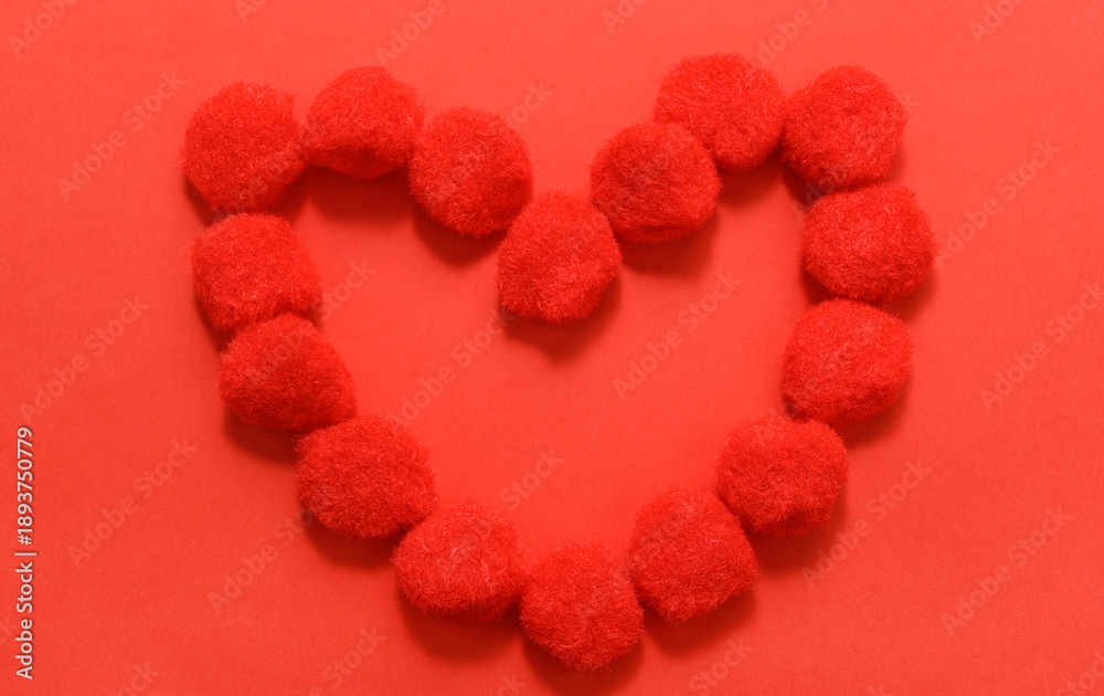 Fototapeta premium The symbol of love is a heart made of pompoms on a red background.