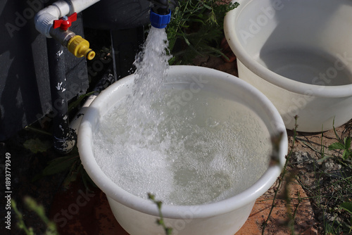 Clear water flowing from an outdoor tap into a plastic bucket, simple household activity in a rural yard, clean water supply for everyday use.