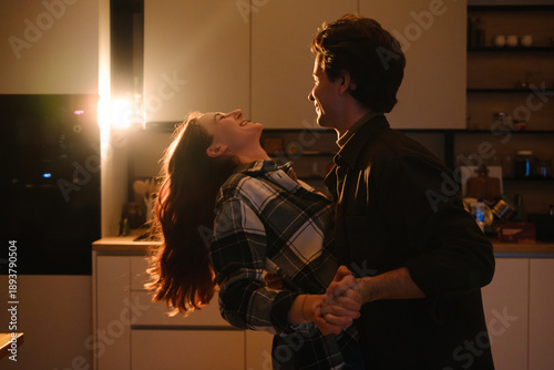 Romantic couple dancing in a warm kitchen at night, smiling and enjoying a playful moment