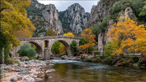 Stone bridge arches across a river with colorful fall foliage and majestic cliffs