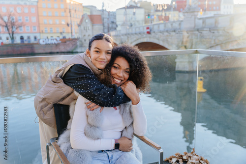Quadro su tela Smiling African American mother and daughter hugging on city bridge in European