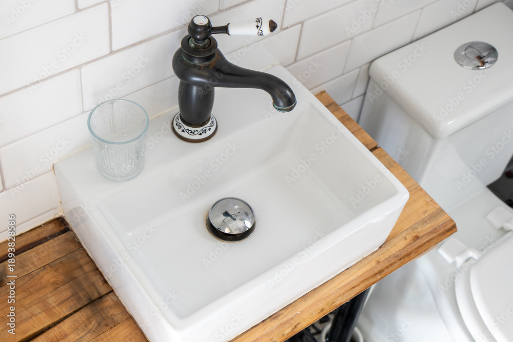Fototapeta premium Modern bathroom interior with white subway tiles, a square ceramic countertop sink, and a black vintage-style faucet with white ceramic details, blending contemporary and retro design