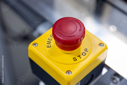 A prominent red emergency stop button mounted on a bright yellow control box, signifying a critical safety feature on industrial machinery.