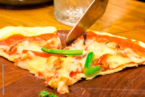 A delicious pizza is being cut on a wooden tray.