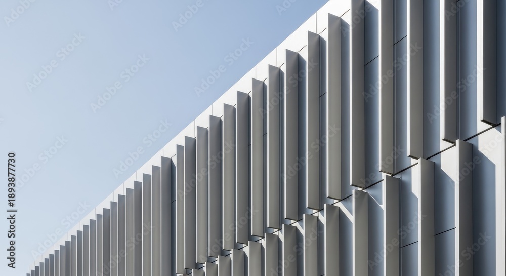 Obraz premium Modern building facade displays repetitive vertical fins against a clear, pale blue sky