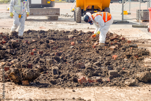 Tableau sur toile Two workers in protective gear remove asbestos from contaminated ground filled w