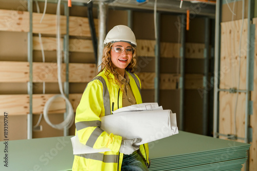 Woman construction worker holds blueprints while standing on  building site