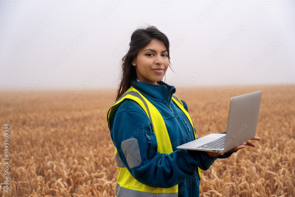 Fototapeta premium Woman farmer or agronomist uses laptop to analyze data in wheat field