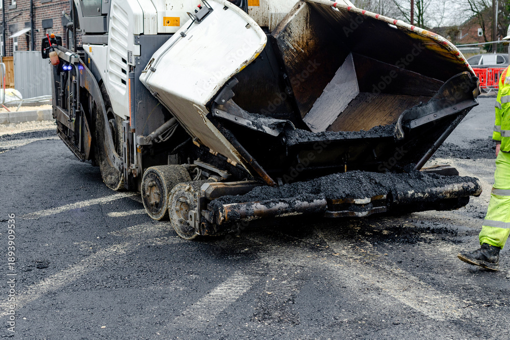 Fototapeta premium Construction workers in high-visibility gear are applyin gfresh hot asphalt to roadway surface