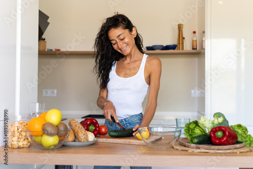 Bilde på lerret Young woman in casual clothes preparing vegetables and fruits in a bright modern kitchen