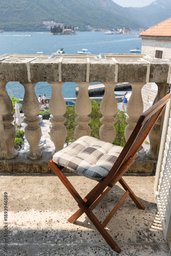 Fototapeta premium A wooden folding chair with a plaid cushion sits on a stone balcony