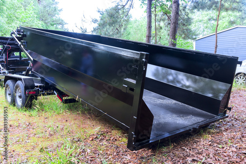 Slika na platnu Waste dump trailer is stationed in woods close to house on clear day
