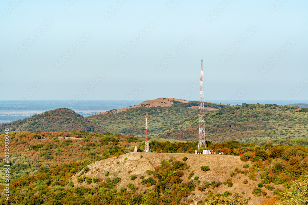 Obraz premium Communication towers on a hilltop surrounded by green hills and clear sky in an open landscape during the day