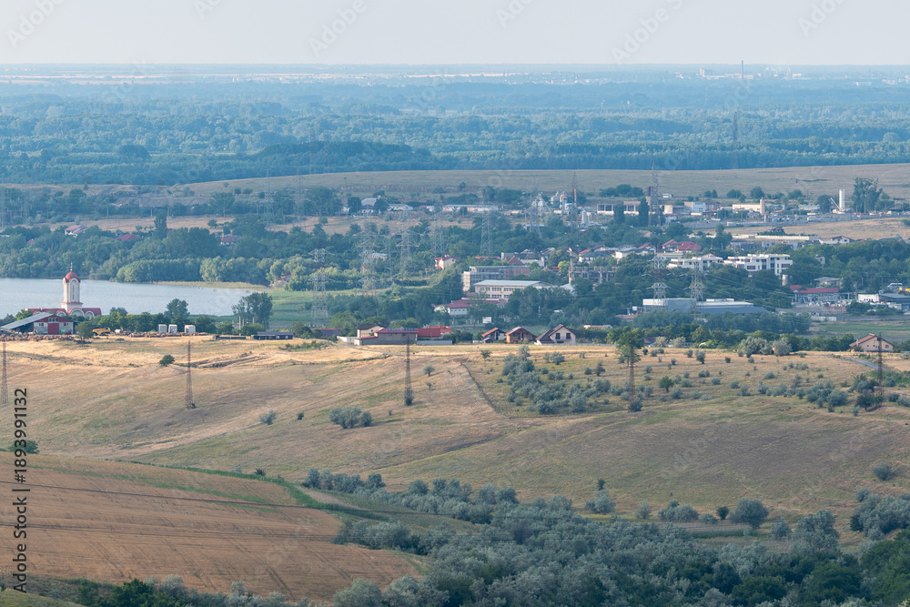 Obraz premium View of a small town by a river surrounded by fields and hills during a clear day in summertime