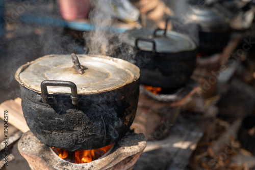 Traditional wood stove cooking with metal pot over fire, rural outdoor kitchen using firewood, sustainable lifestyle, simple living and traditional food preparation