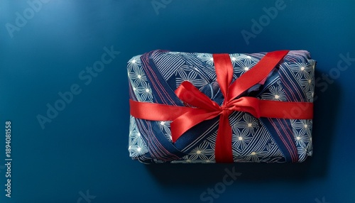 Gift Wrapped In Furoshiki Fabric With Traditional Japanese Patterns And Red Ribbon On Dark Blue Background In Minimalist Style With Copy Space Christmas Banner