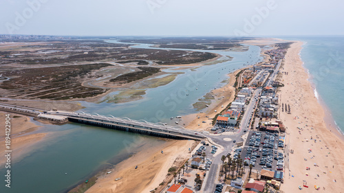 Aerial perspective shows Praia de Faro with new bridge and surrounding landscape with water bodies, beach area, and vehicles parked near the shoreline in Portugal