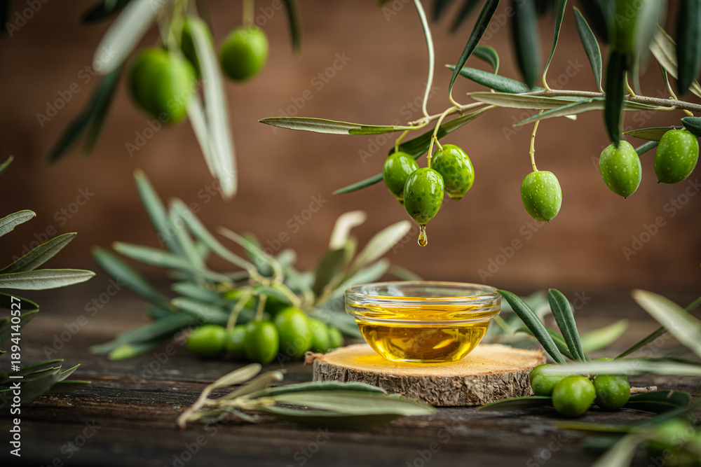Naklejka premium Small glass bowl filled with olive oil placed on wooden surface surrounded by fresh green olives and olive branches. Concept of Mediterranean cuisine, organic farming, healthy food and natural harvest